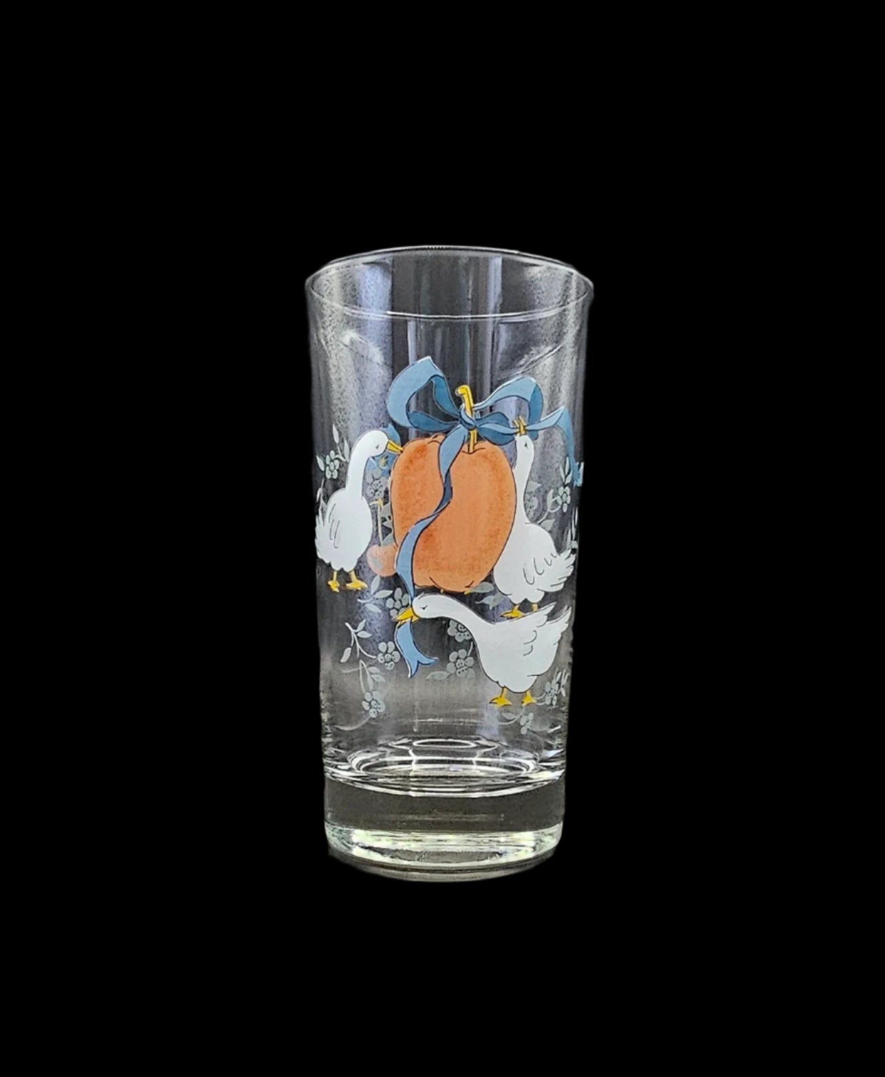 12 Oz Marmalade Water Glass or Tumbler. Photo shows three white geese surrounding a red apple with a blue ribbon tied around its stem and flowing around the geese.